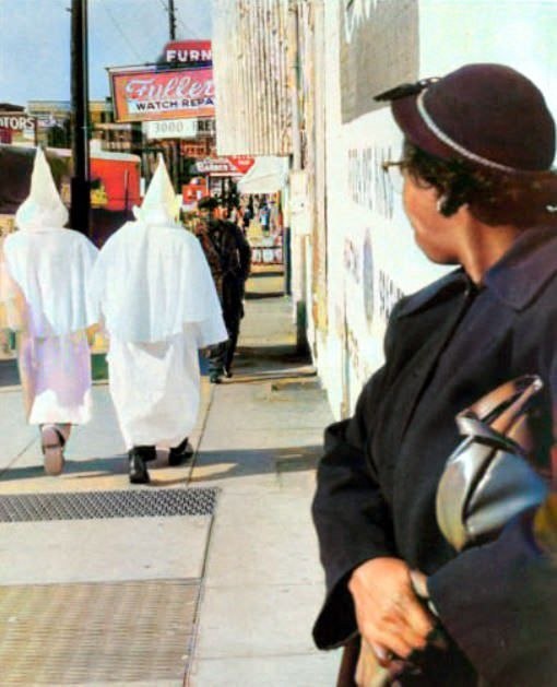 Женщина наблюдает за тем, как члены ку-клукс-клана в масках идут по центру Монтгомери, штат Алабама, перед митингом, который состоялся в тот вечер, 24 ноября 1956 года