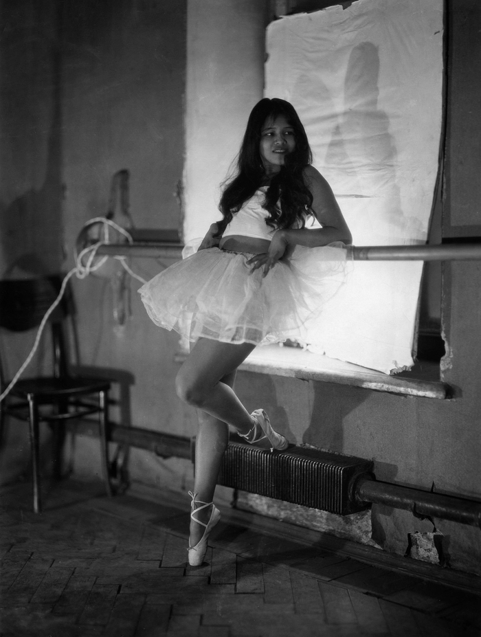 Ученица в балетках и кружевной юбке опирается на станок